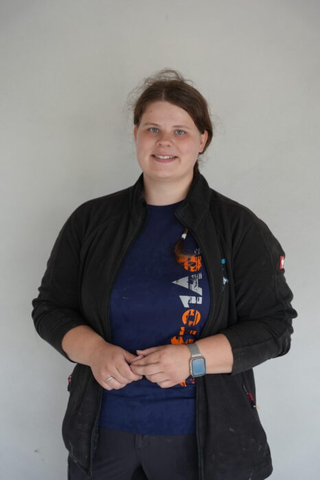 Das Bild zeigt eine junge Frau vor einer weißen Wand stehend. Es handelt sich dabei um die Auszubildende Fliesenlegerin Isabelle