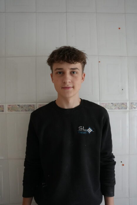 Das Bild zeigt einen jungen Mann vor einer weißen Wand stehend. Es handelt sich dabei um den Auszubildenden Fliesenleger Anton